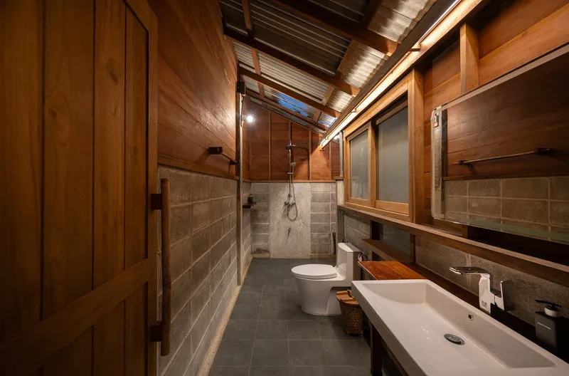 Bathroom interior with grey concrete block walls, timber ceiling, clerestory window, and wall-mounted timber basin