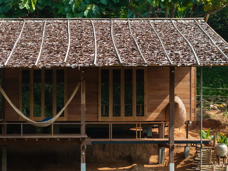 Timber pavilion with thatched roof and open wooden slat walls under afternoon sun
