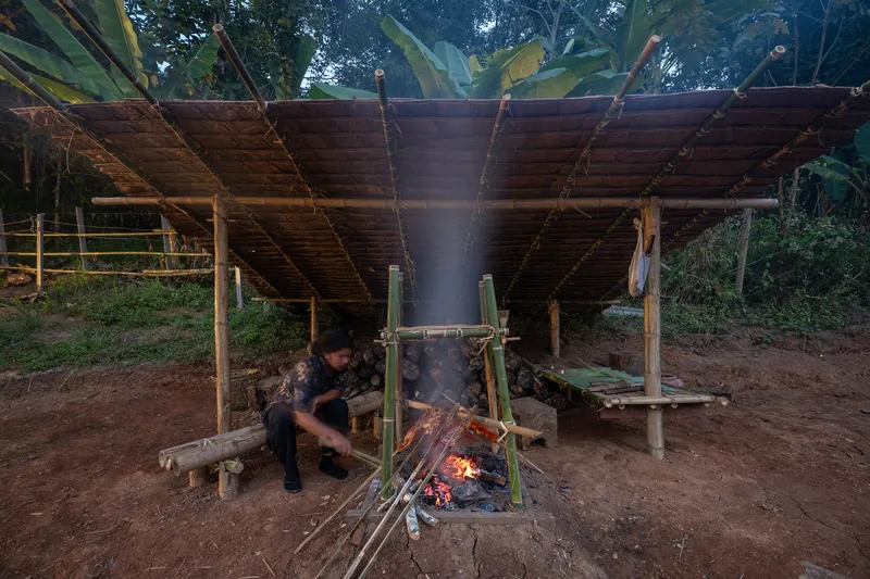 Covered cooking area with timber posts and plank roof showing suspended bamboo grill over open fire