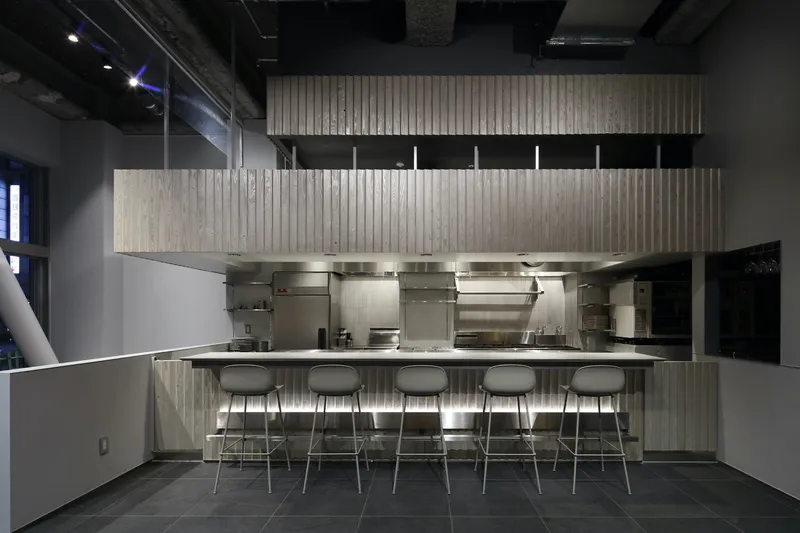 Commercial kitchen with stainless steel equipment, vertical timber cladding, and bar seating facing the counter