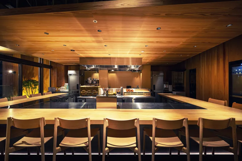 Dining counter with timber ceiling and chairs beneath warm downlighting at night