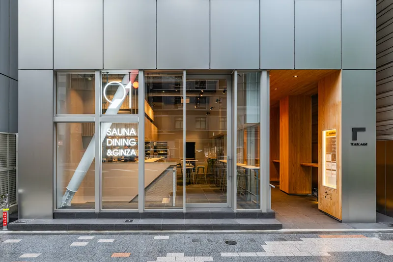 Street-level entrance with grey panel facade, full-height glazing, and timber-lined doorway at twilight