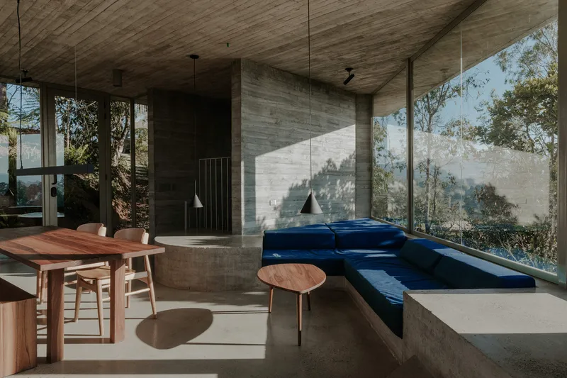 Living space with board-formed concrete walls, timber ceiling, and blue upholstered built-in seating catching afternoon sun