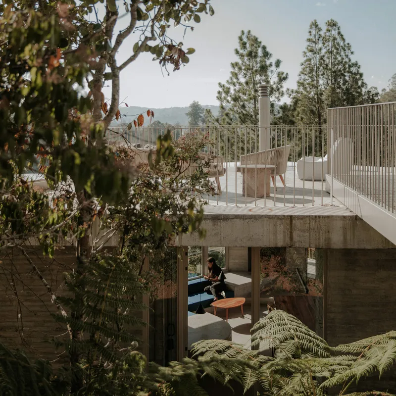 Concrete roof terrace with vertical metal railing and white seating framed by surrounding trees and ferns