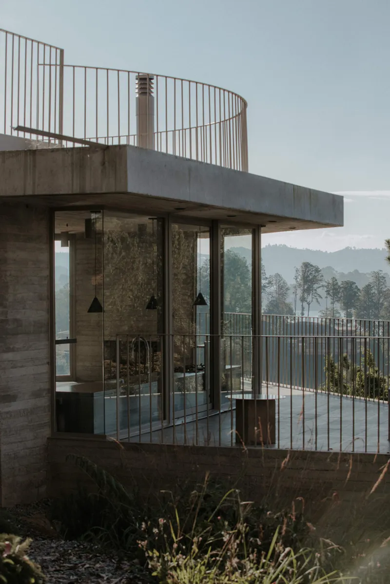Glass corner volume with board-formed concrete walls topped by a curved metal railing terrace overlooking misty hills
