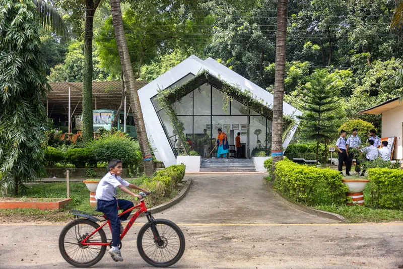 Angular white pavilion with glazed gable and planted green roof as a child cycles past