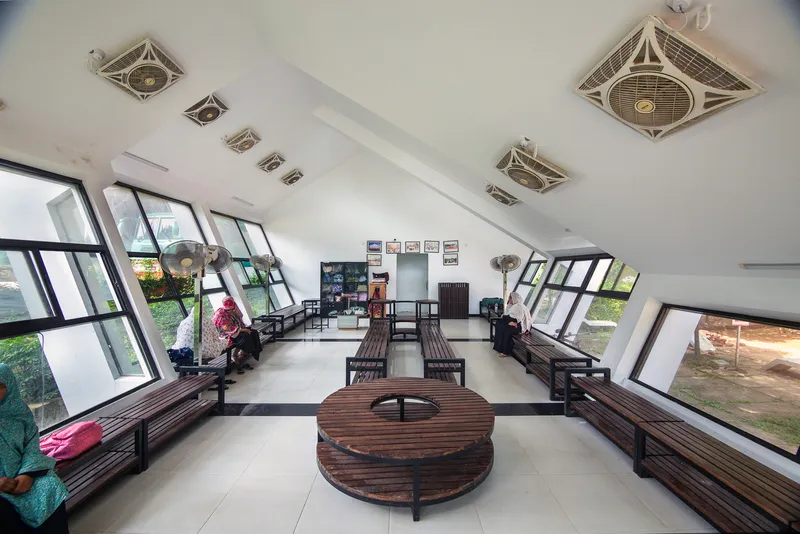 Interior with wooden seating platforms and circular table beneath ceiling fans and sloped glazing