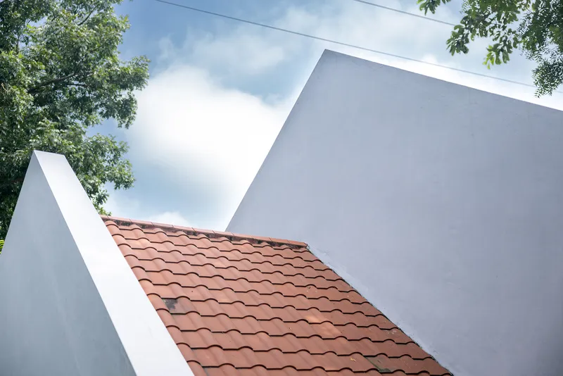 Clay tile roof sloping between two white stucco walls framed by leafy branches above