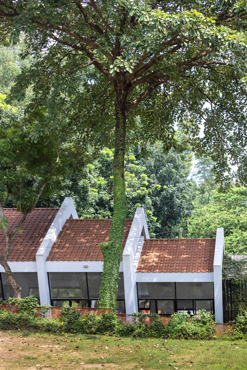 Three gabled roof volumes with terracotta tiles nestled beneath a canopy of mature trees