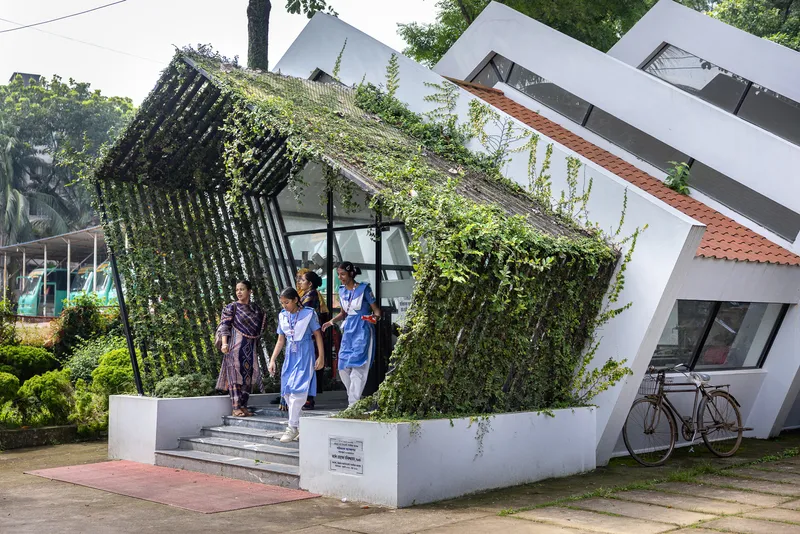 Steps leading to glazed entrance beneath vegetated steel trellis on raised white plinth with visitors exiting