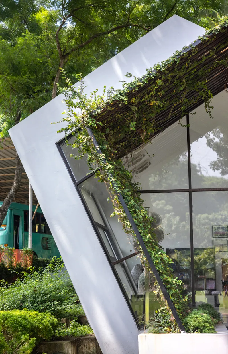 Vertical planted trellis with climbing vines rising along glazed facade beneath canopy of trees