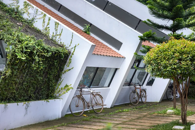 Angled white facade with terracotta tile roof detail and bicycles parked along the garden path