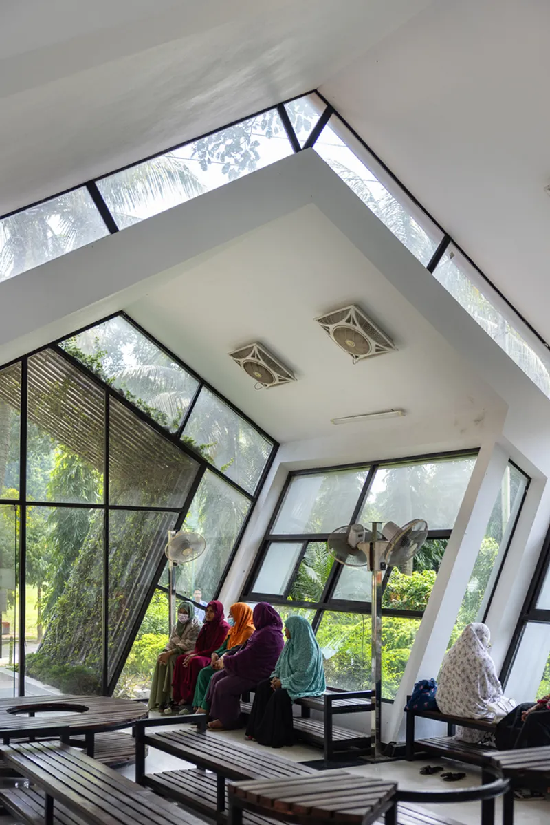 Interior space with sloped ceiling and angled windows where visitors in colorful clothing sit on low wooden platforms