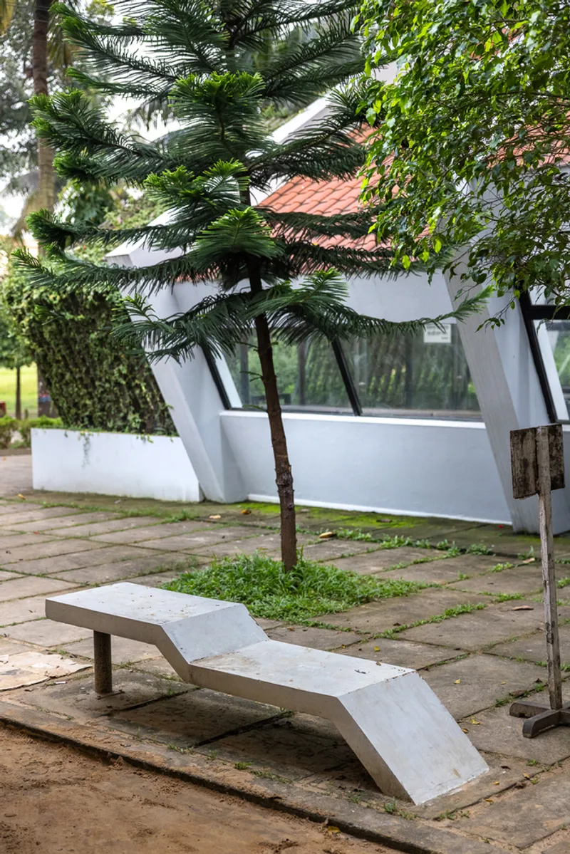 Precast concrete lounge chair beneath a palm tree in the paved courtyard