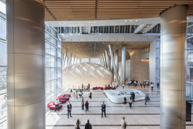 Double-height lobby with angled white columns supporting a timber batten ceiling above scattered visitors
