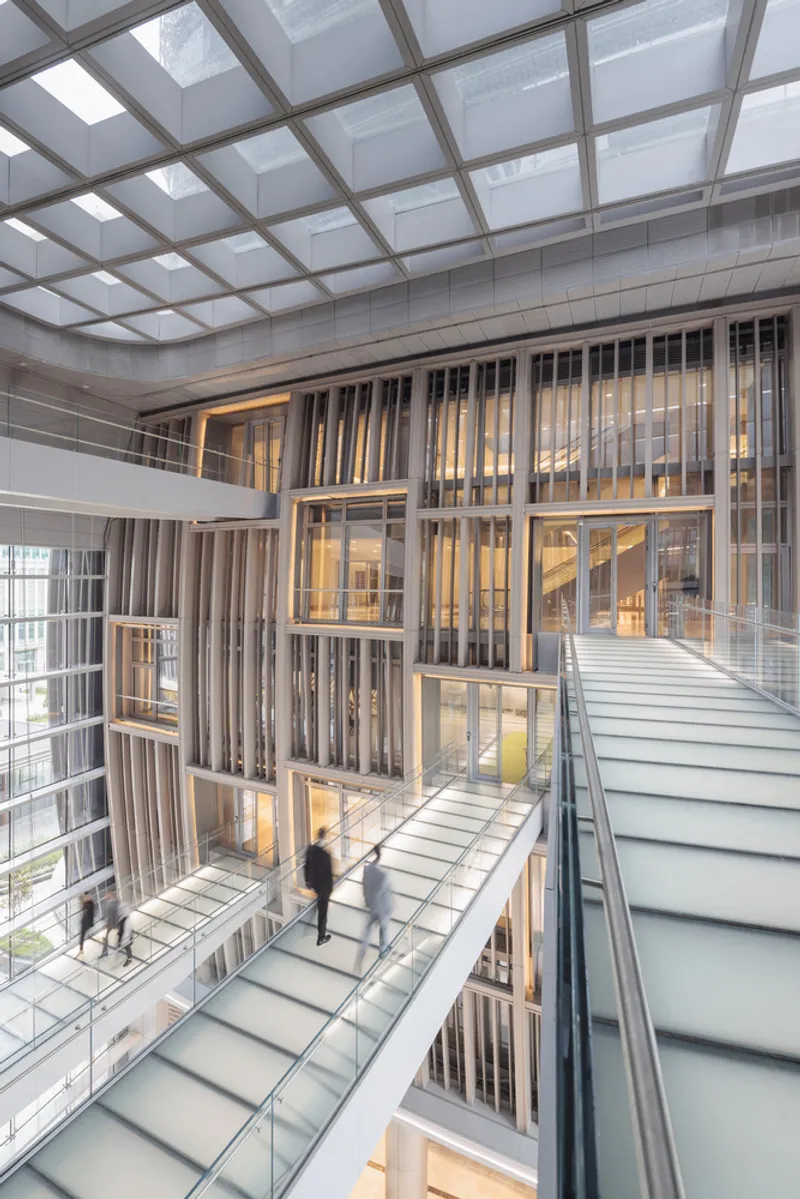 Multi-level glass-floored atrium with translucent ceiling grid and a figure crossing the floor
