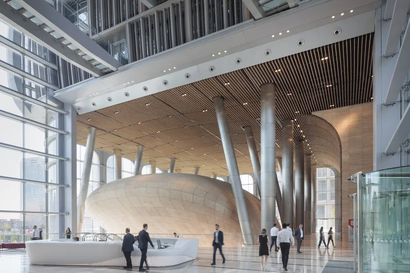 Lobby with curving stone wall beneath white branching columns and timber-slatted ceiling with business people walking