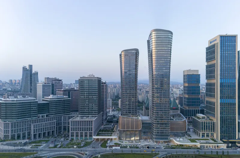 Aerial view of twin cylindrical towers and podium within the dense urban skyline at twilight