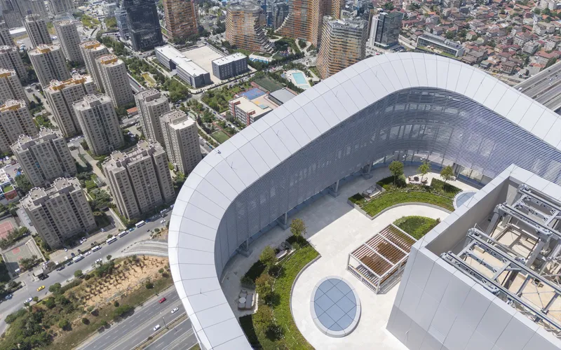 Drone view of a curved white roof with rooftop gardens and an oval skylight among urban towers