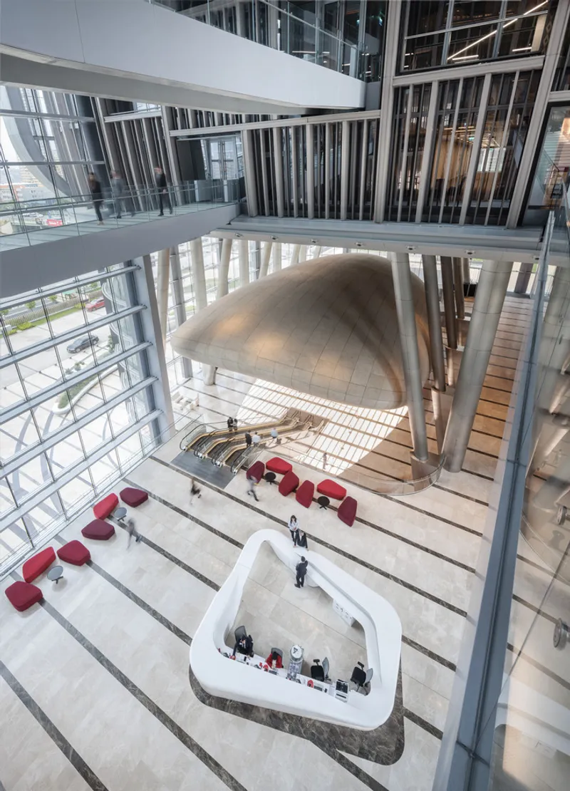 Multi-story atrium with white balconies, sculptural ceiling volume, and red seating below