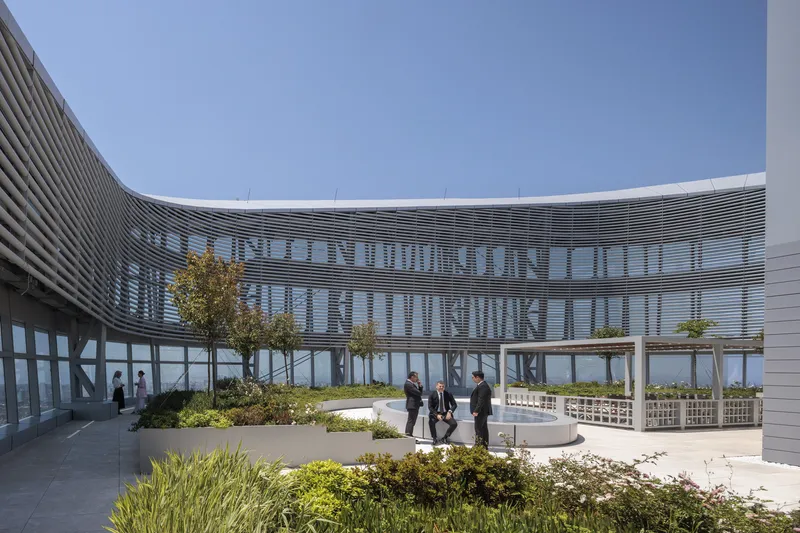 Rooftop terrace with planted beds and a timber pergola overlooking a curved horizontal louver facade