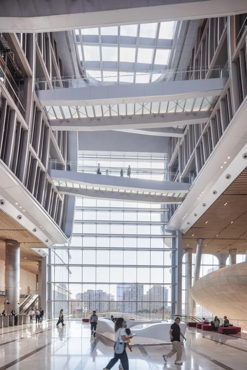 Atrium interior with white steel bridges crossing between floors beneath a glazed curtain wall