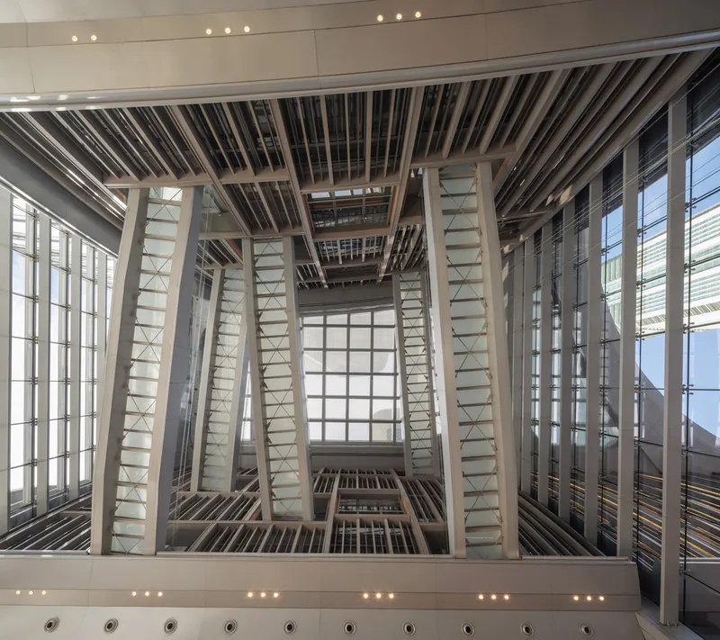 Upward view into a rectangular atrium framed by white structural beams and horizontal louvres