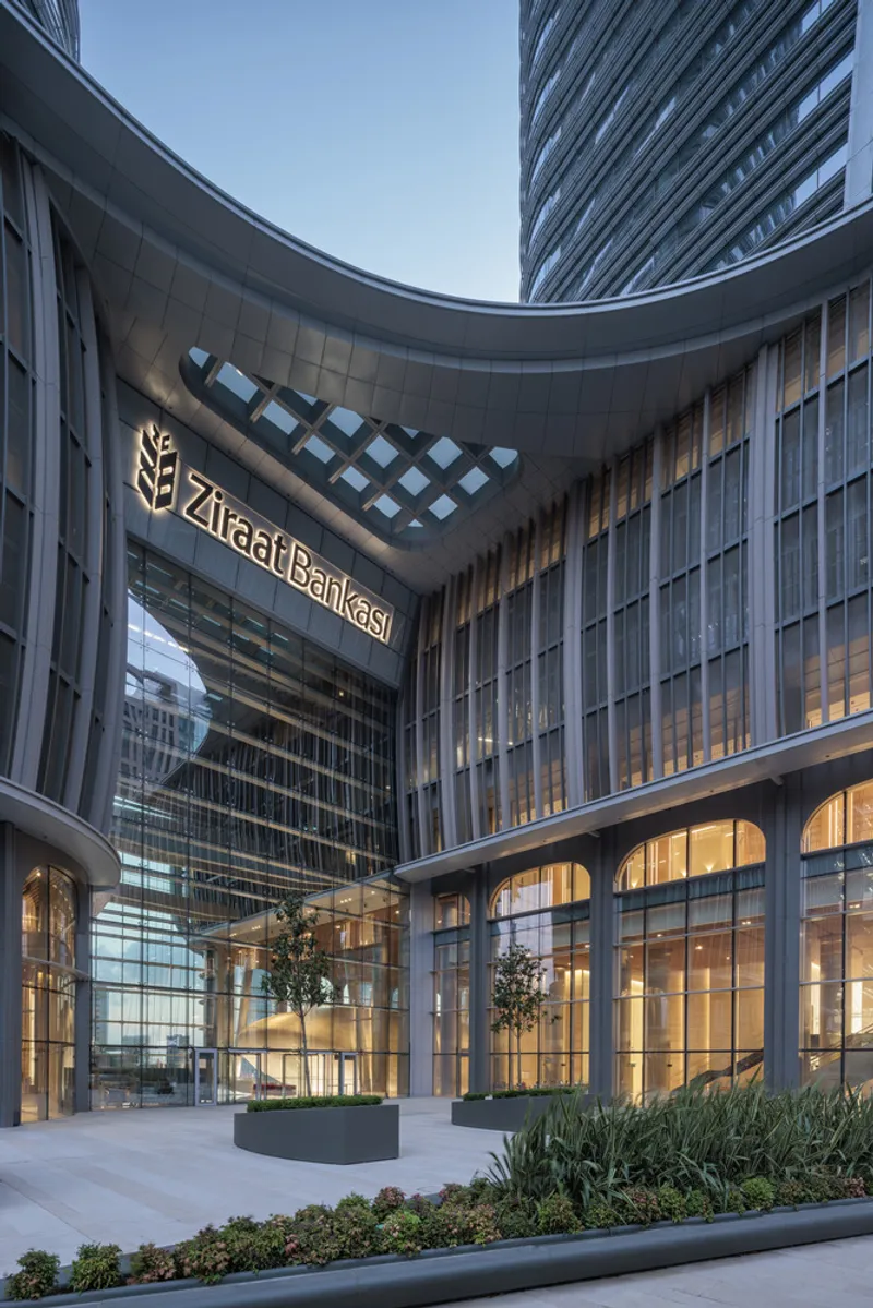Glazed courtyard between tower volumes with planted beds and trees at dusk