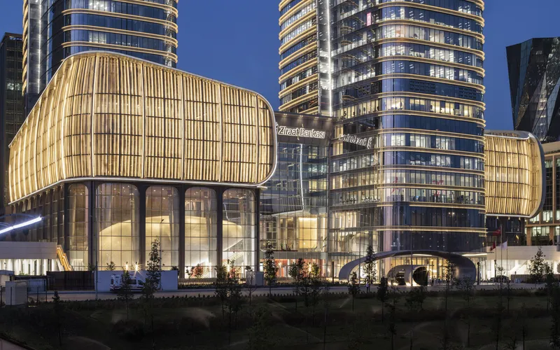 Illuminated podium facades with vertical metal fins alongside glass towers at blue hour