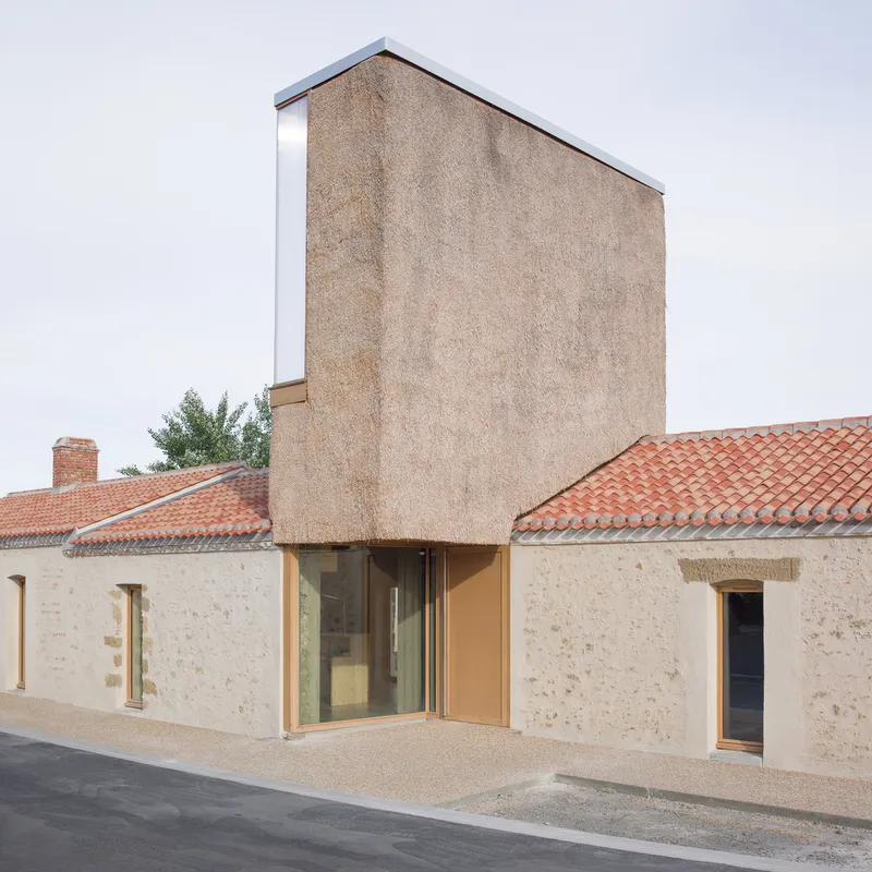Street facade showing a recessed glazed entry between stone walls topped with terracotta tiled roofs