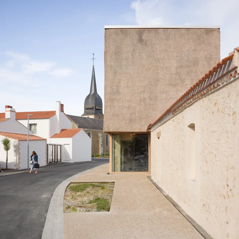 Courtyard view with glazed entry, concrete tower and church spire visible beyond the stone walls