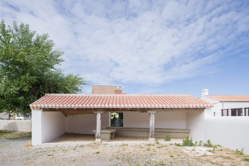 Covered porch with white columns, terracotta barrel tile roof, and concrete bench on gravel ground