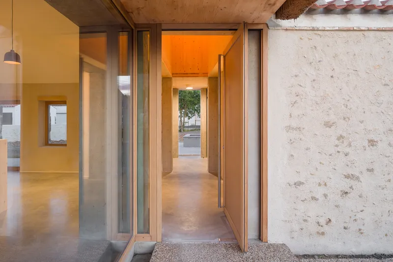 Entry threshold with timber-framed glass door and exposed plywood ceiling illuminated at dusk