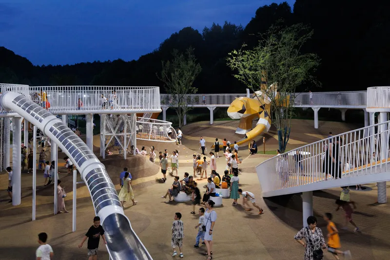 White elevated walkways and tube slide surrounding a yellow sculptural element at dusk