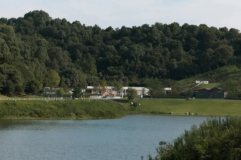 View across the lake showing the playground and support facilities set against a wooded hillside
