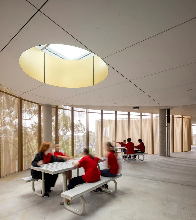 Interior common space with circular skylight and students in red uniforms at bench tables