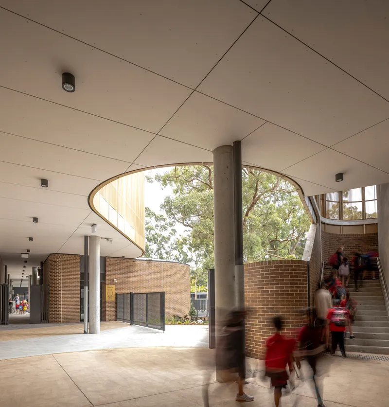 Covered entry hall with paneled ceiling, concrete columns, and staircase as students move through the space