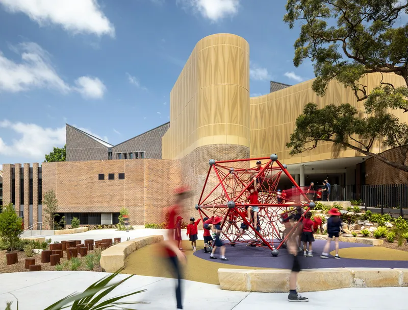 Exterior courtyard with red climbing structure in front of cylindrical tower and brick facades under blue sky