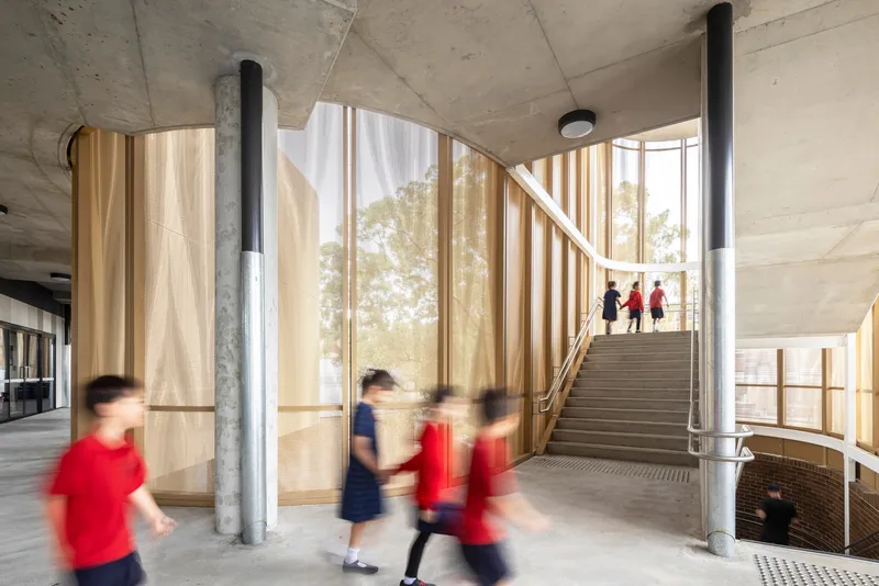 Concrete interior staircase with timber-clad curved walls and students in red uniforms moving through space