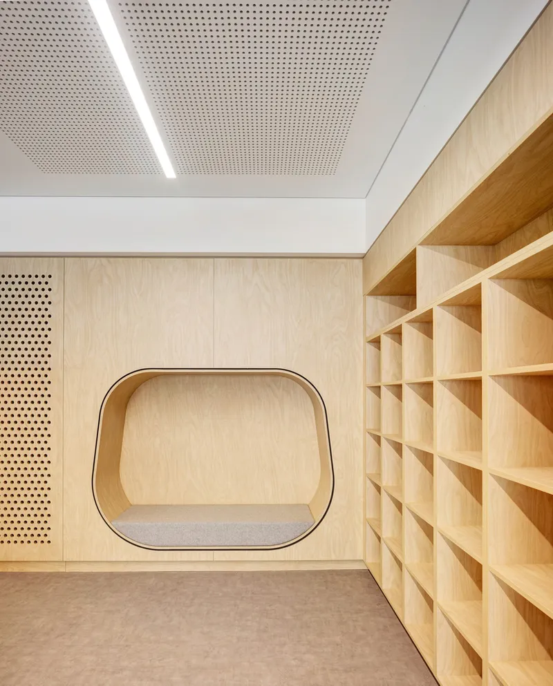 Timber-lined room with perforated acoustic ceiling and rounded nook in pale plywood shelving