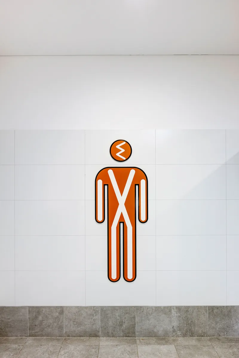 Orange and white indigenous figure icon mounted on white tile wall above grey stone flooring