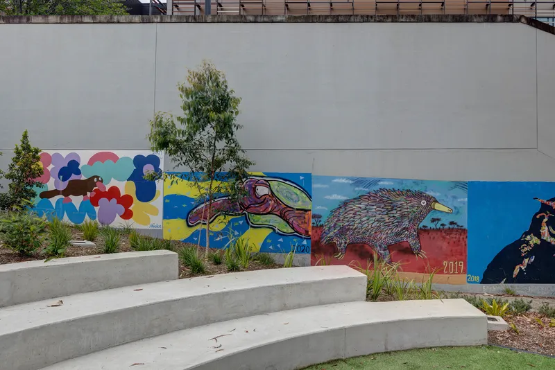 Concrete outdoor seating steps beside planted beds and mural wall with indigenous animal artwork