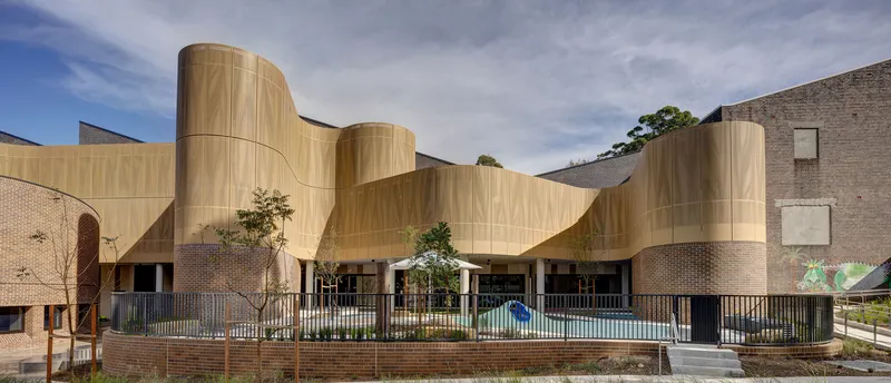 Undulating timber-clad facade with cylindrical towers above a brick base and planted courtyard