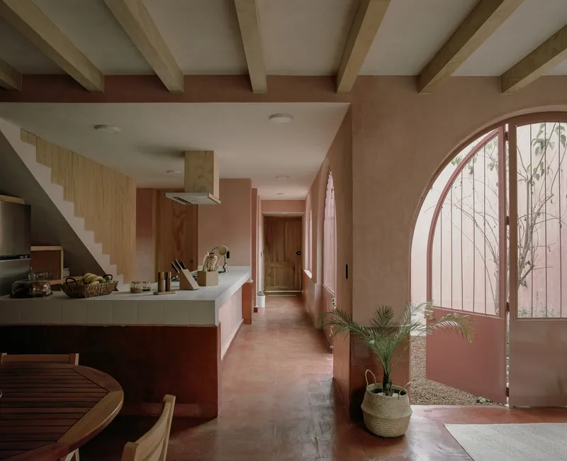 Kitchen and dining area with exposed timber ceiling beams and arched window opening onto a planted courtyard