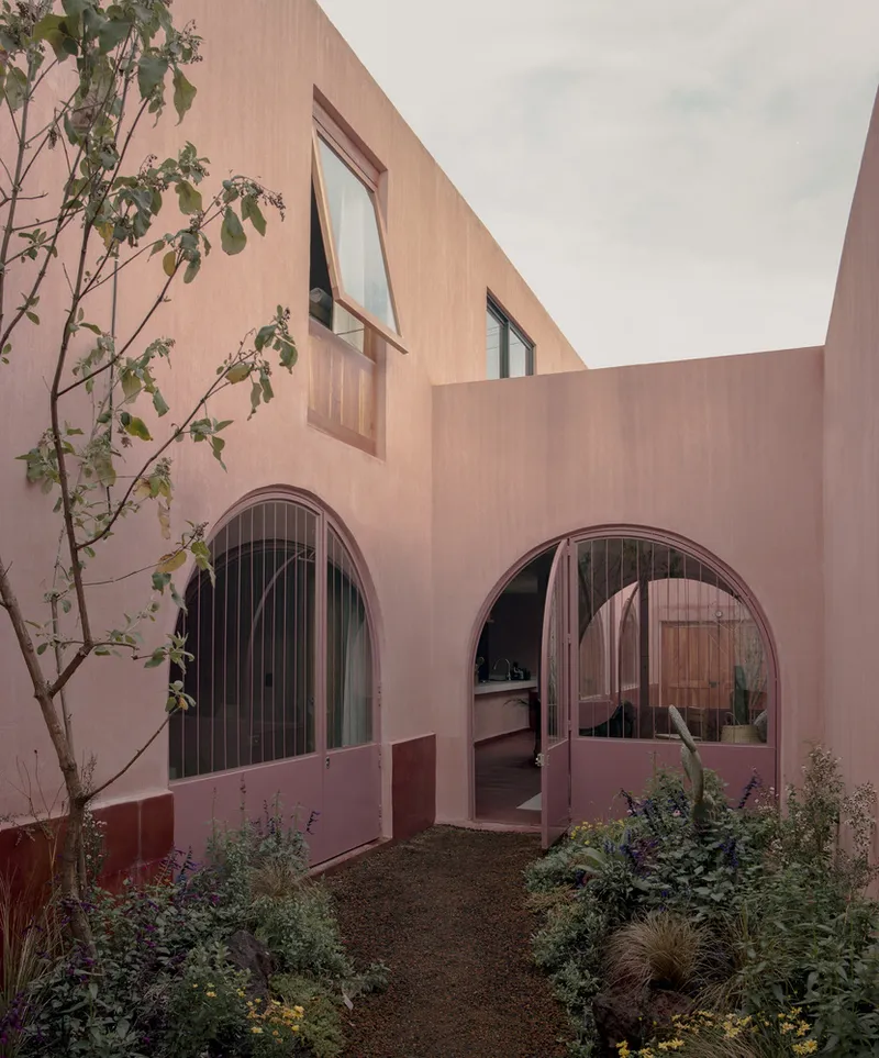 Planted courtyard showing two arched openings and a small tree against pink rendered facades