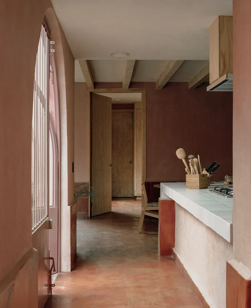 Kitchen with timber ceiling beams and vertical slat window filtering daylight along pink walls