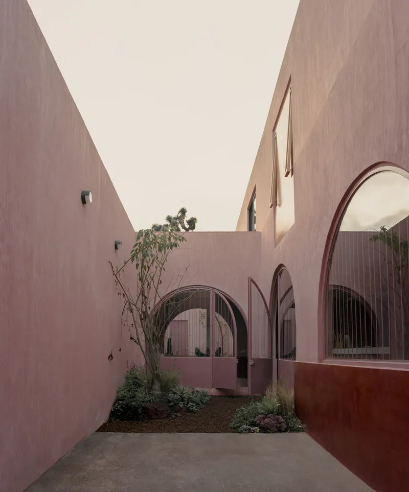 Courtyard with arched glazed openings and planted garden bed beneath pink rendered walls