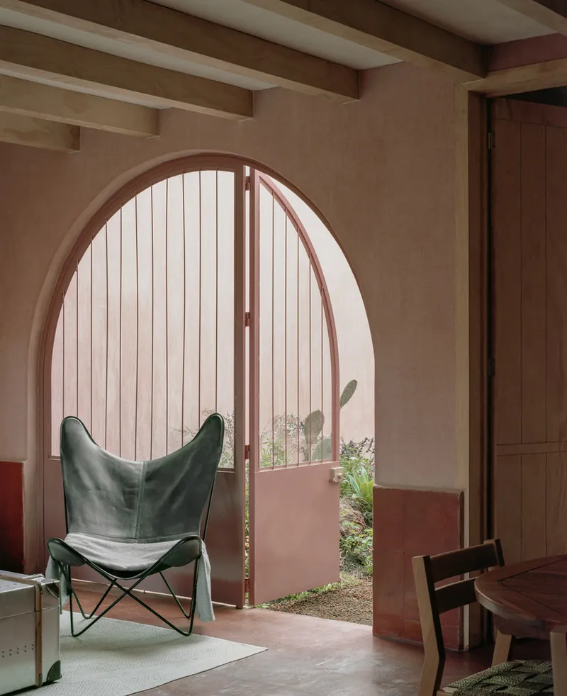 Interior arched doorway with vertical slat door opening to a planted courtyard with butterfly chair