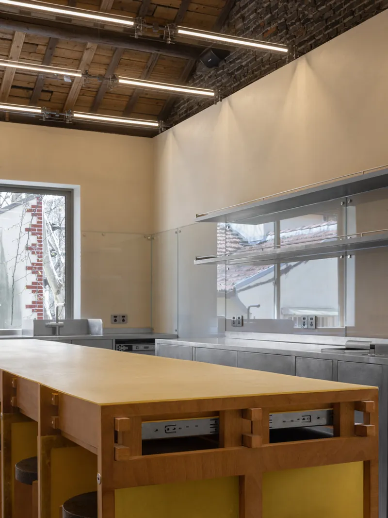 Kitchen workspace with exposed brick ceiling and timber island beneath linear fluorescent lighting fixtures