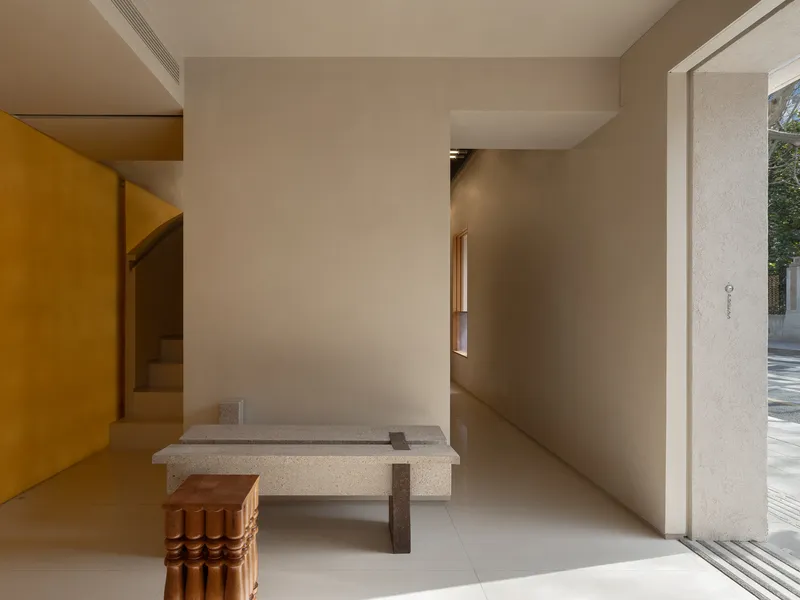 Interior hallway showing terrazzo bench with timber stool beside yellow stairwell and open doorway